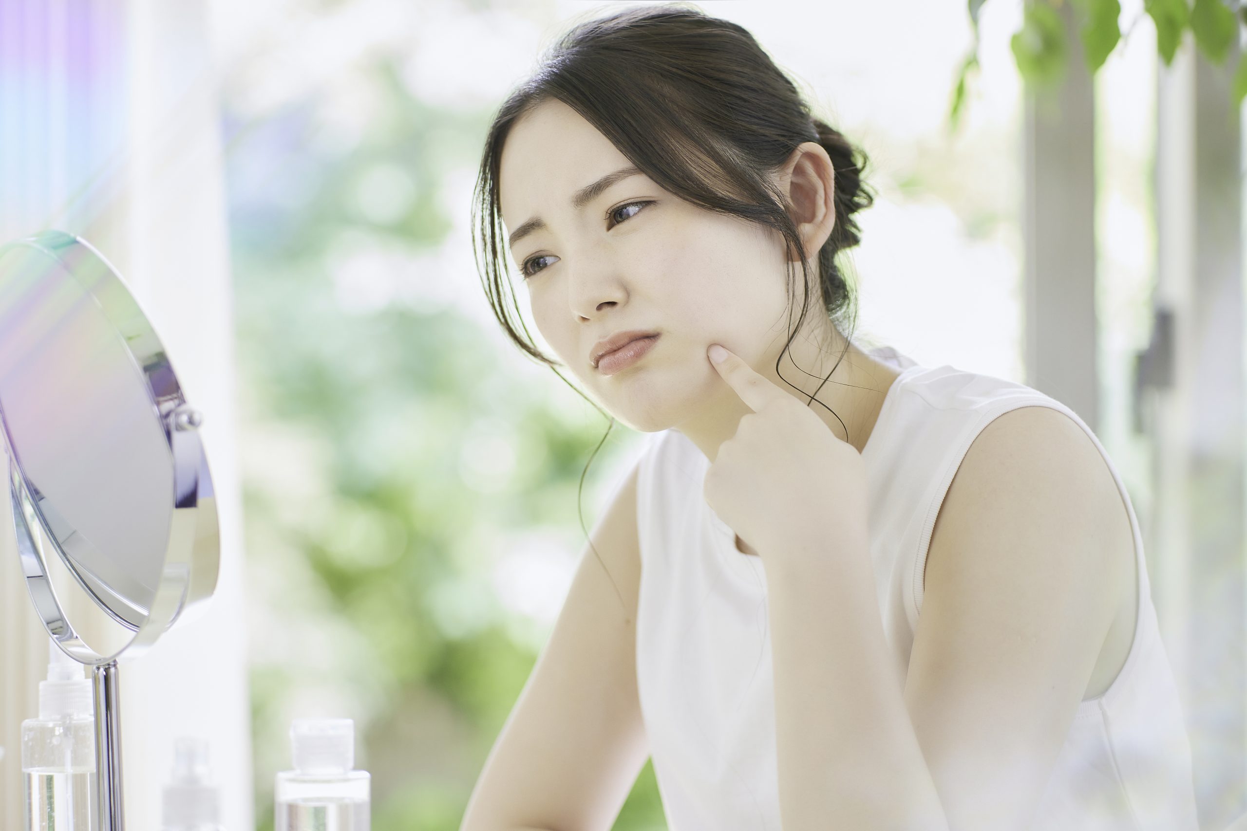 鏡で自分の肌を見て悩む女性