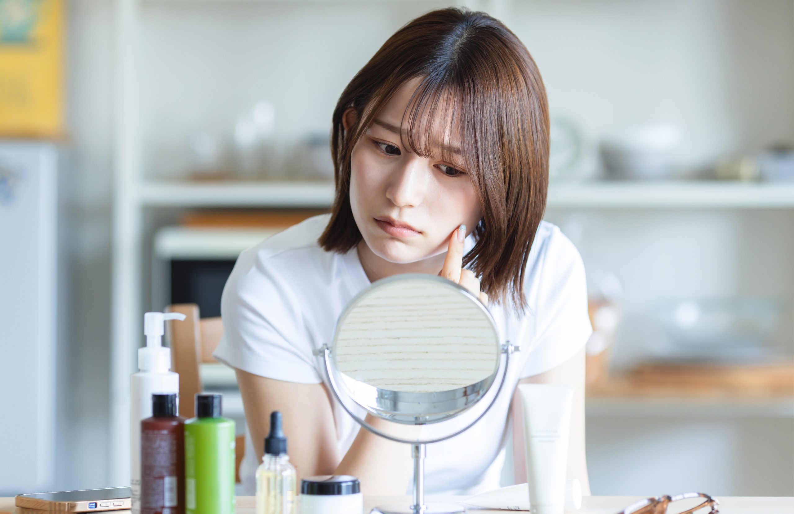 鏡で自分の肌を見て悩む女性